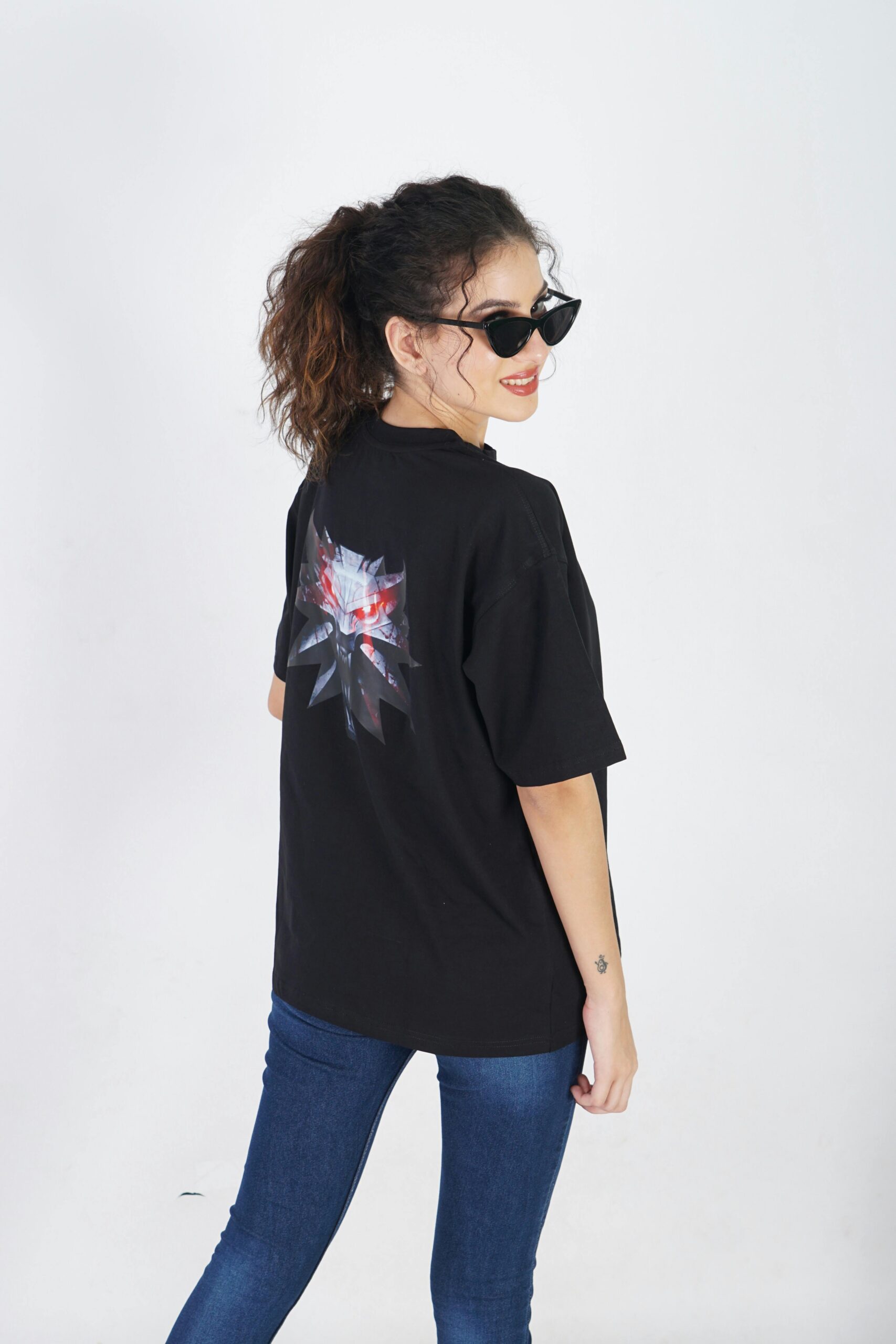 Stylish woman in sunglasses poses in a graphic t-shirt and jeans in a studio setting.