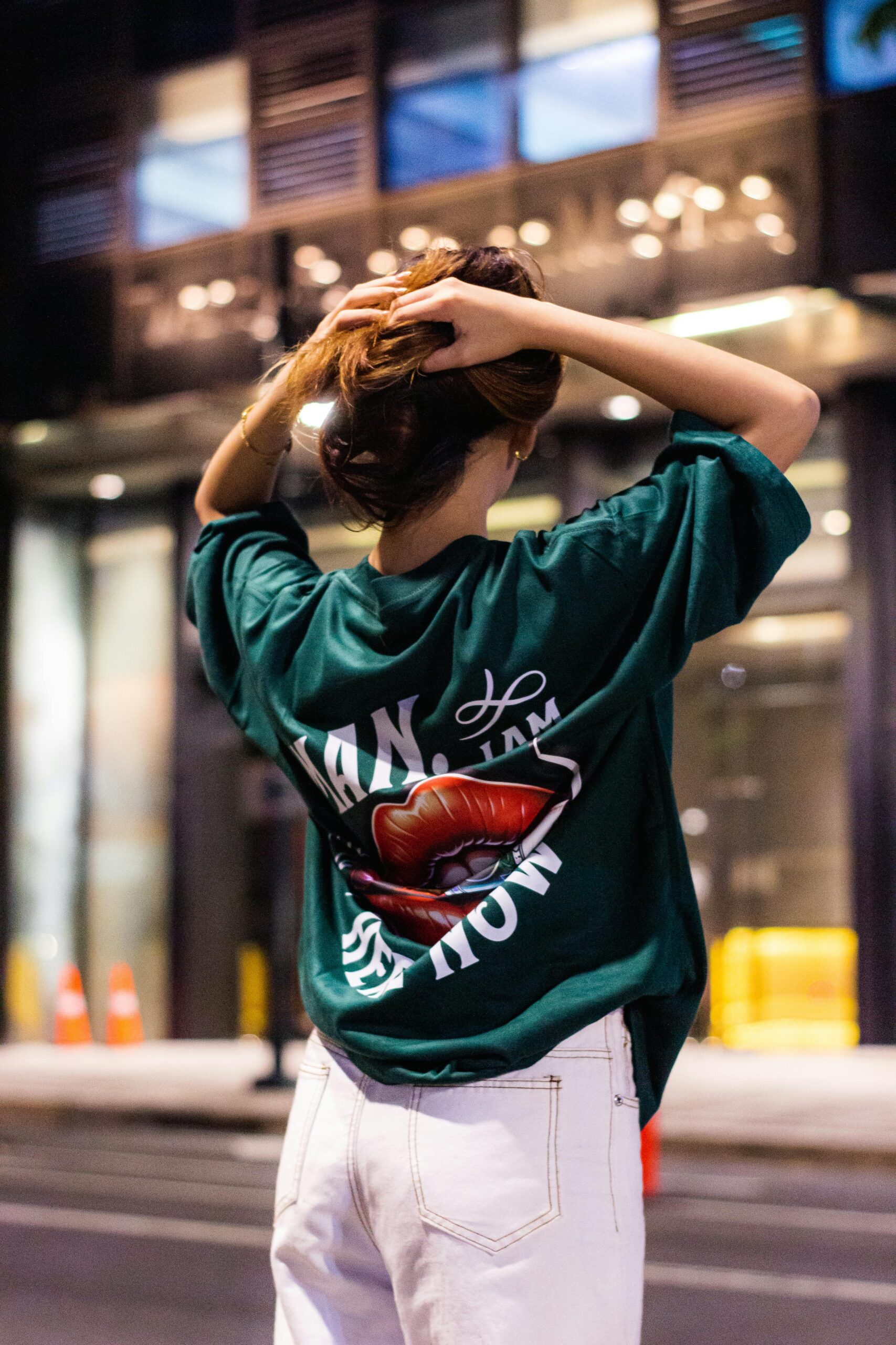 Trendy woman in oversized t-shirt posing outdoors at night in a vibrant city setting.