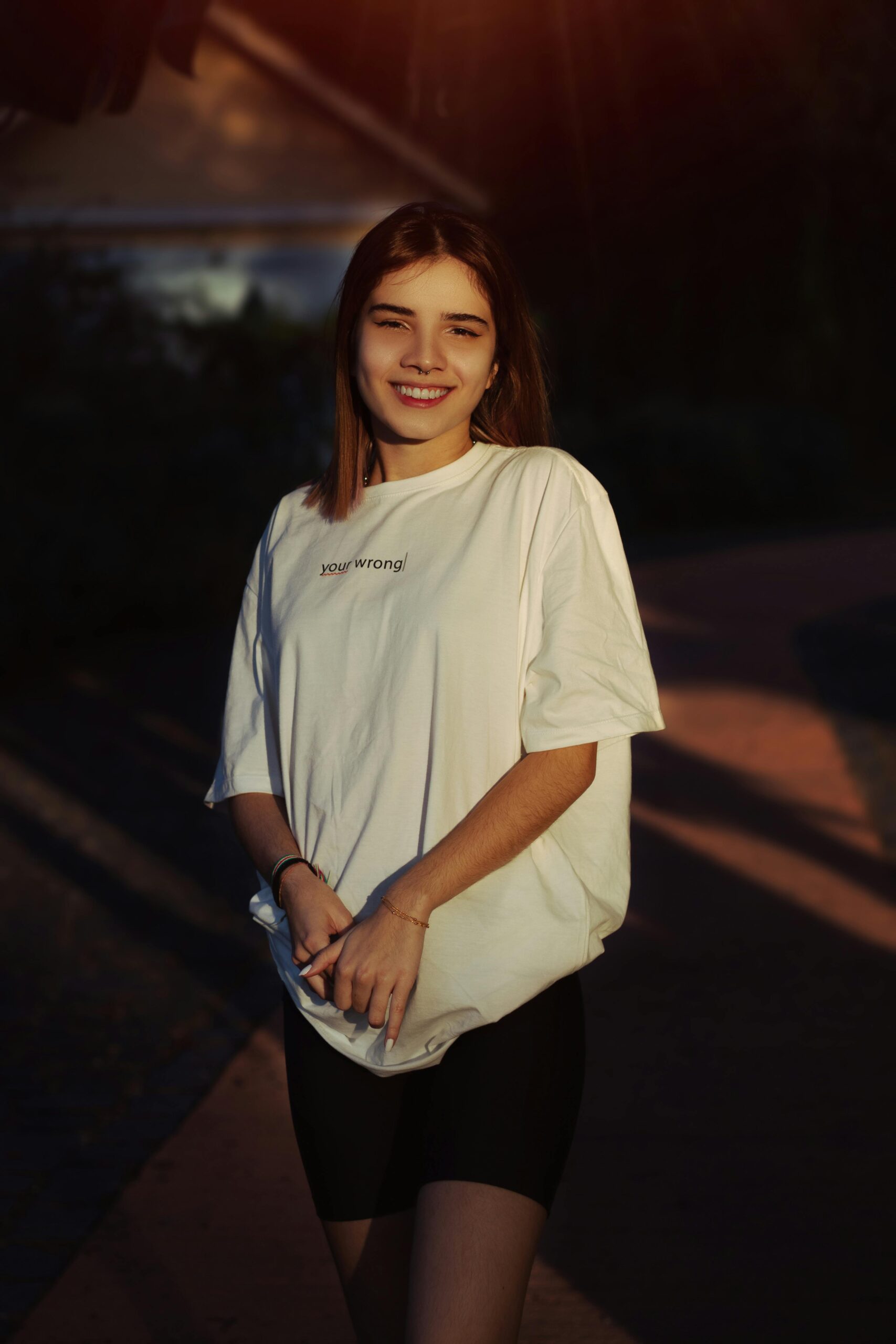A smiling young woman in a loose t-shirt enjoys a sunny day outdoors, casting a relaxed and happy vibe.